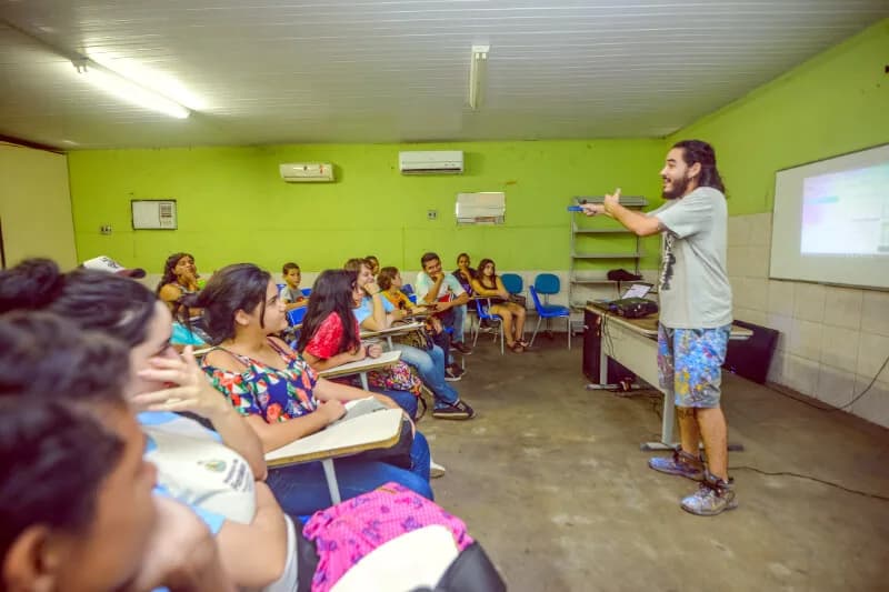 Oficina em sala de aula: rapaz apresenta em pé para estudantes sentados nas carteiras, case HOUSECULTURA