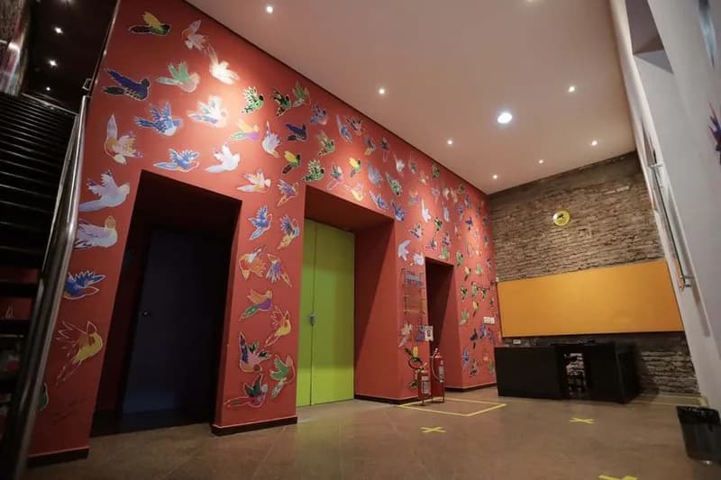 Saguão da Casa da Ribeira com parede laranja coberta de pássaros pintados, case HOUSECULTURA
