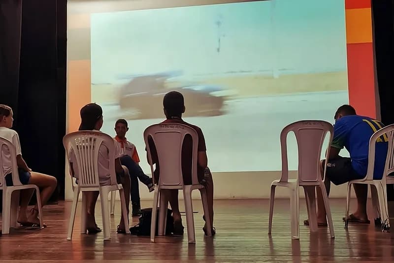 Jovens sentados assistem a uma projeção de vídeo em sala escura do Porto de Ama, case HOUSECULTURA