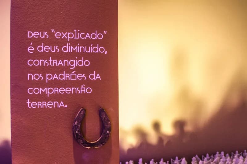 Painel do módulo de religiosidade com frase em letras rosa e ferradura fixada, exposição O Tempo Eu e Vc, case HOUSECULTURA