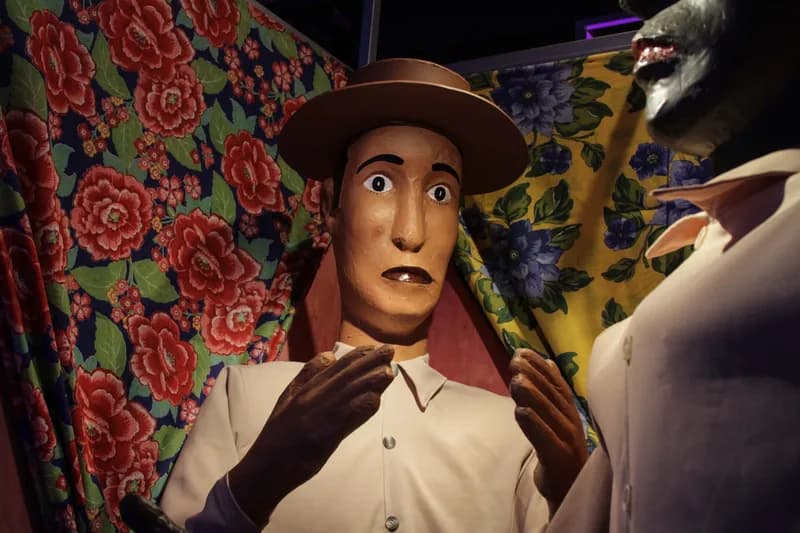 Boneco de mamulengo com chapéu diante de tecidos floridos na exposição O Tempo Eu e Vc, case HOUSECULTURA