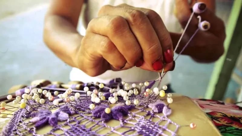 Mãos de rendeira fixam alfinetes e linha sobre a almofada de renda, websérie DôMóValô da HOUSECULTURA