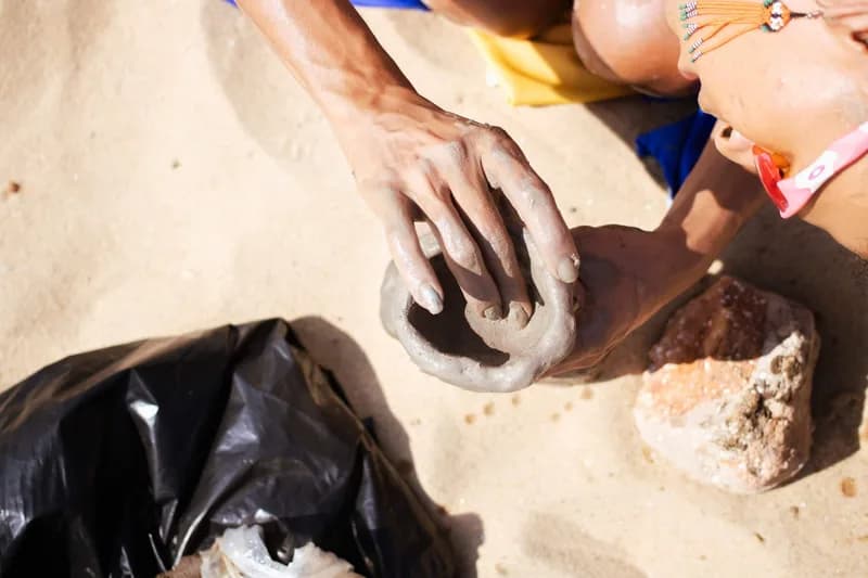 Mãos de criança modelam argila na areia da praia durante o festival Arte Praia, case HOUSECULTURA