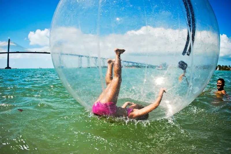 Pessoa dentro de bola inflável transparente flutuando no mar durante o festival Arte Praia, case HOUSECULTURA