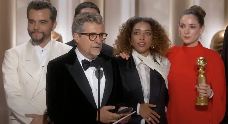 Equipe de O Agente Secreto no palco de premiação, com discurso ao microfone e estatueta em mãos, case HOUSECULTURA