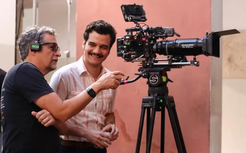 Bastidores da filmagem de O Agente Secreto: diretor e ator ao lado da câmera no tripé, case HOUSECULTURA